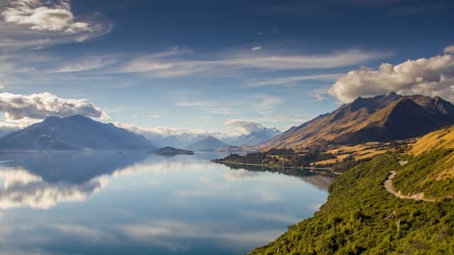 Tranquil New Zealand lake perfectly reflecting snow-capped mountains under dramatic sky