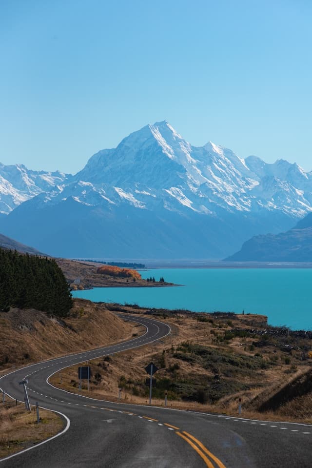 Winding mountain highway alongside turquoise lake with Mount Cook in distance
