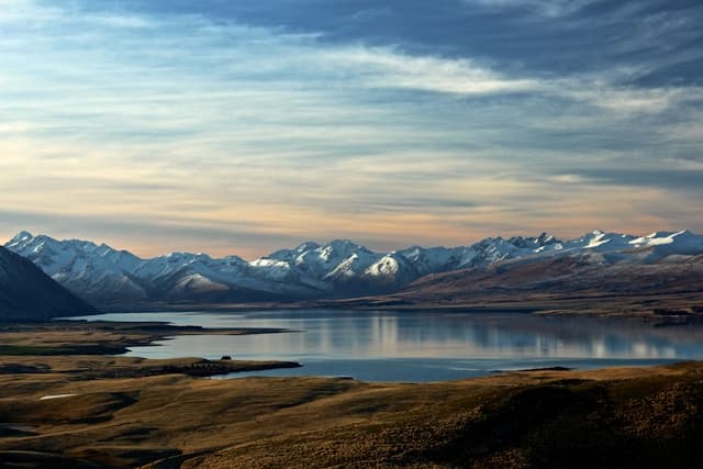 Panoramic view of snow-capped New Zealand mountains reflected in tranquil lake at golden hour
